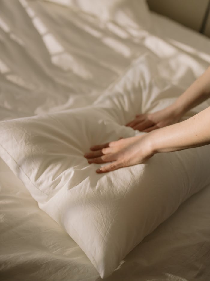 A close-up of hands arranging a pillow on a neatly made bed, creating a cozy atmosphere.